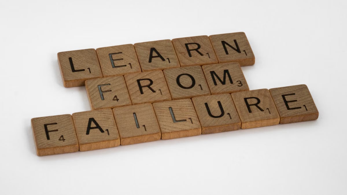 Wooden Scrabble tiles spelling 'Learn from Failure' on a white background, promoting resilience.